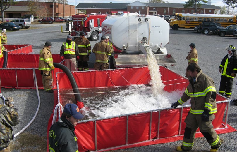 A large water tanker dumps water into a Husky folding frame tank during a water shuttle operation