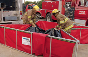 Firefighters folding up a Husky® standard folding frame tank using Easy Lift Handles